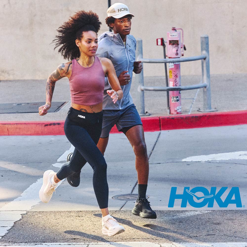 Two people running on a street with Hoka branding.