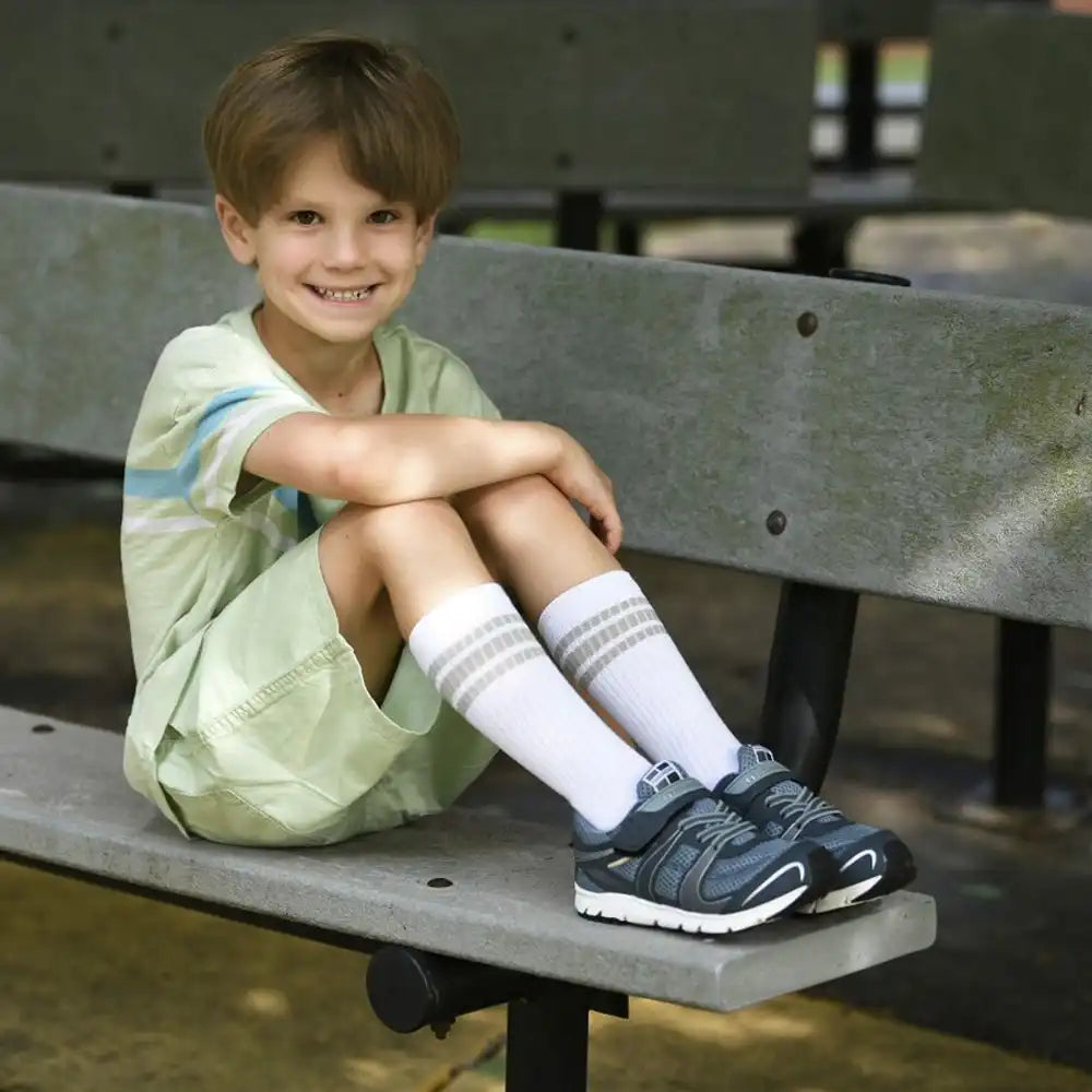 Child sitting on a bench wearing a light green dress, white socks, and gray sneakers.