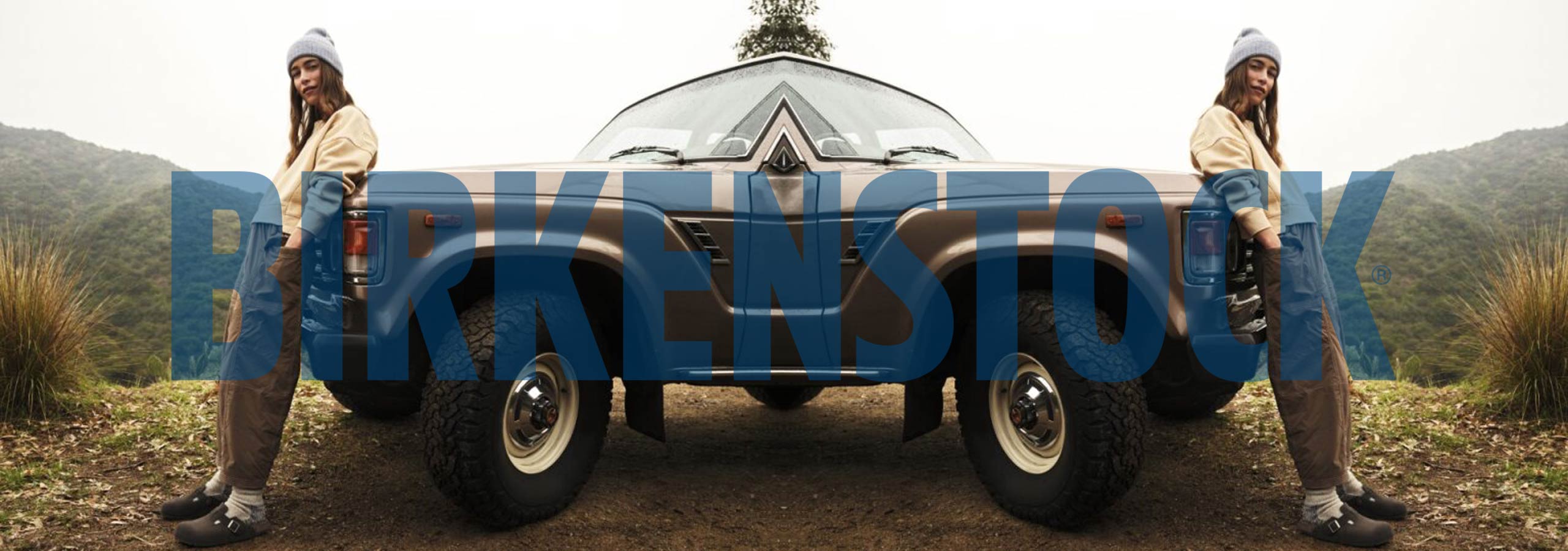 Two people sitting on a vintage camper van with 'Barkenstock' branding in a scenic outdoor setting.