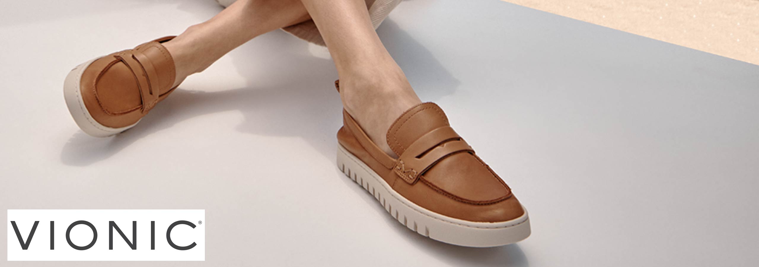Brown loafers worn by a person on a light gray surface with 'Vionic' branding.