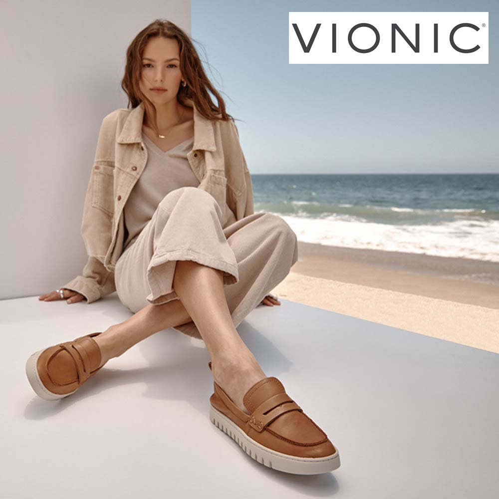 Woman wearing Vionic shoes sitting by a beach with 'Vionic' branding.